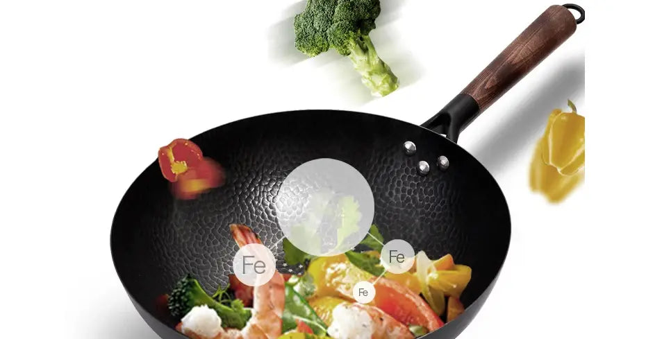 Wok de hierro artesanal de acero negro estampado a martillo con asa de madera, que contiene camarones y verduras.