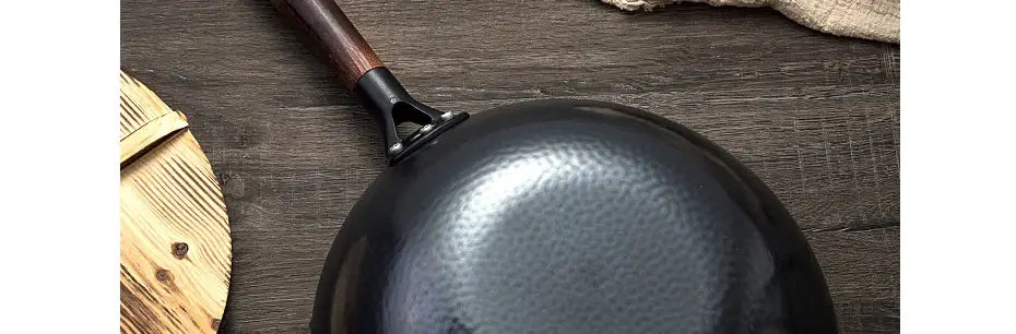 Wok de acero negro estampado a martillo con asa de madera oscura, destacado como parte de una colección de un wok de hierro hecho a mano con asa de madera y tapa de vidrio.