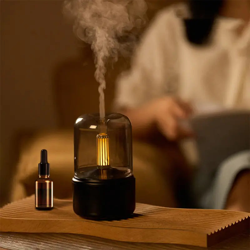A sleek black candle light aroma diffuser usb humidifier with a glass dome and glowing golden filament emitting mist with a 120ml capacity.