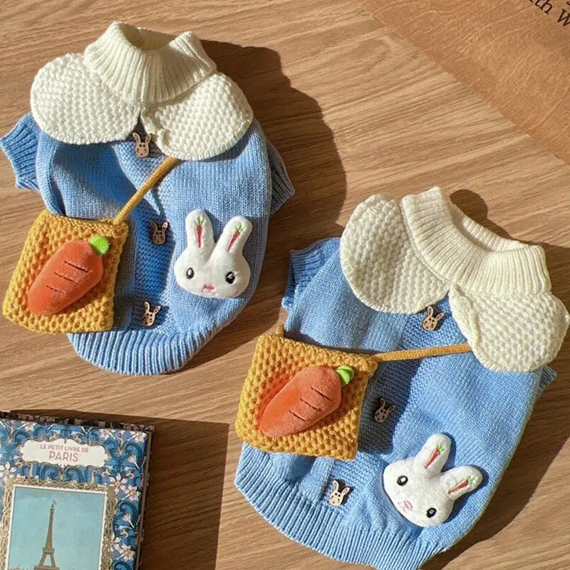 Le pull pour animal de compagnie en tricot représentant un lapin bleu présente un tissu en maille bleue avec un col blanc et une pochette bandoulière à thème de carotte pour les animaux.