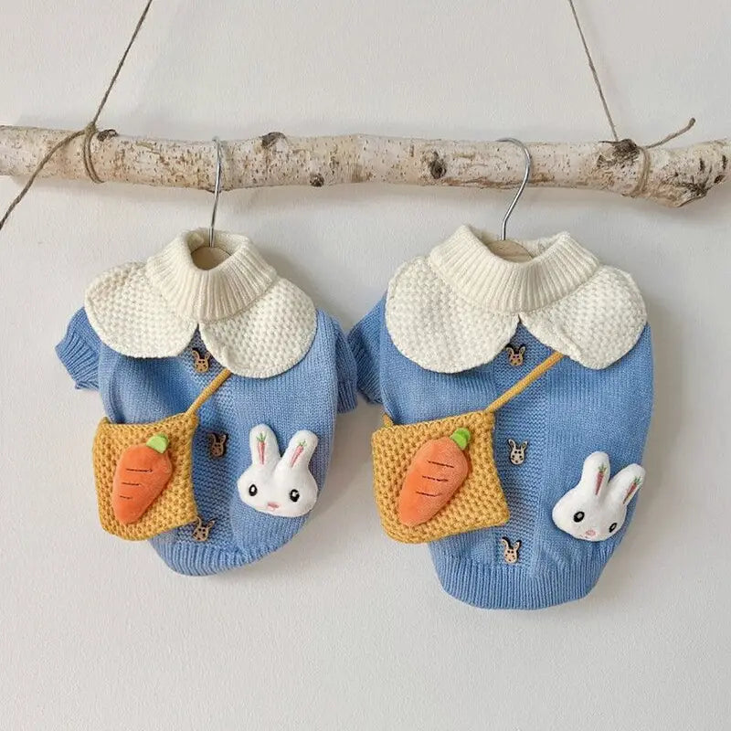 Pull pour animal de compagnie en tricot représentant un lapin bleu, réalisé dans une matière tricot bleu, avec un col texturé blanc et des poches jaunes comportant des carottes brodées et des appliqués de lapin.