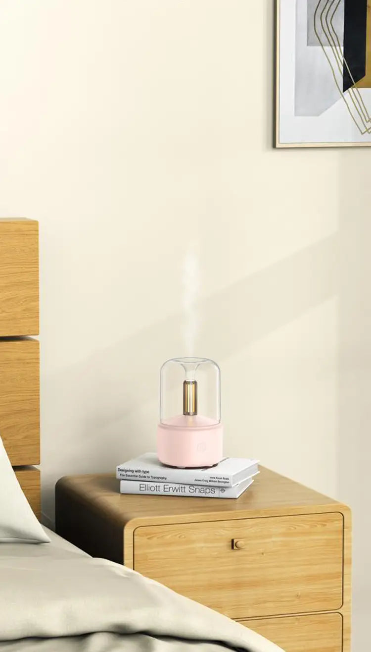 pink glass candlelight aroma diffuser usb mist humidifier with gold-colored central element sitting on stacked books on wooden nightstand