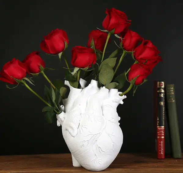 White anatomical heart-shaped vase made of nordic resin sculpture holding vibrant red roses as a decorative flower pot.