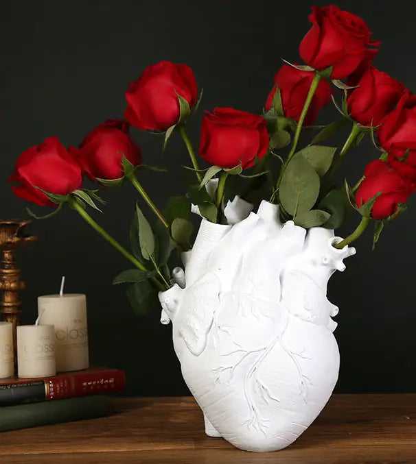 White anatomical heart shaped nordic resin sculpture vase holding vibrant red roses for flower display.