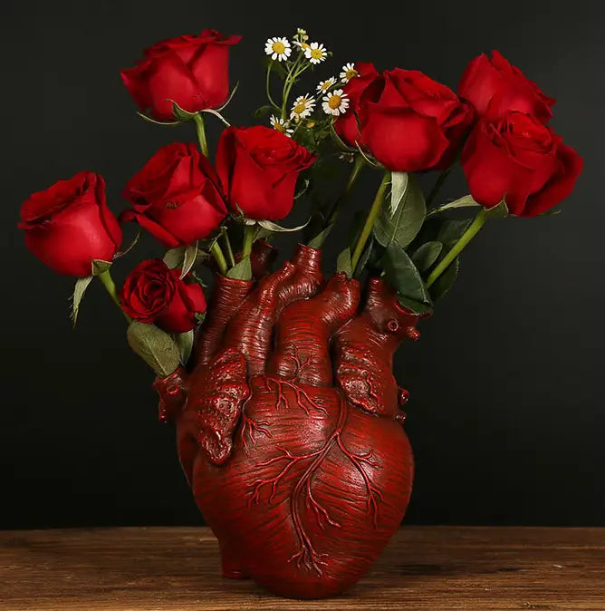 a glossy red anatomical heart vase made of nordic resin holding vibrant red roses and delicate white daisies as a decorative flower pot.