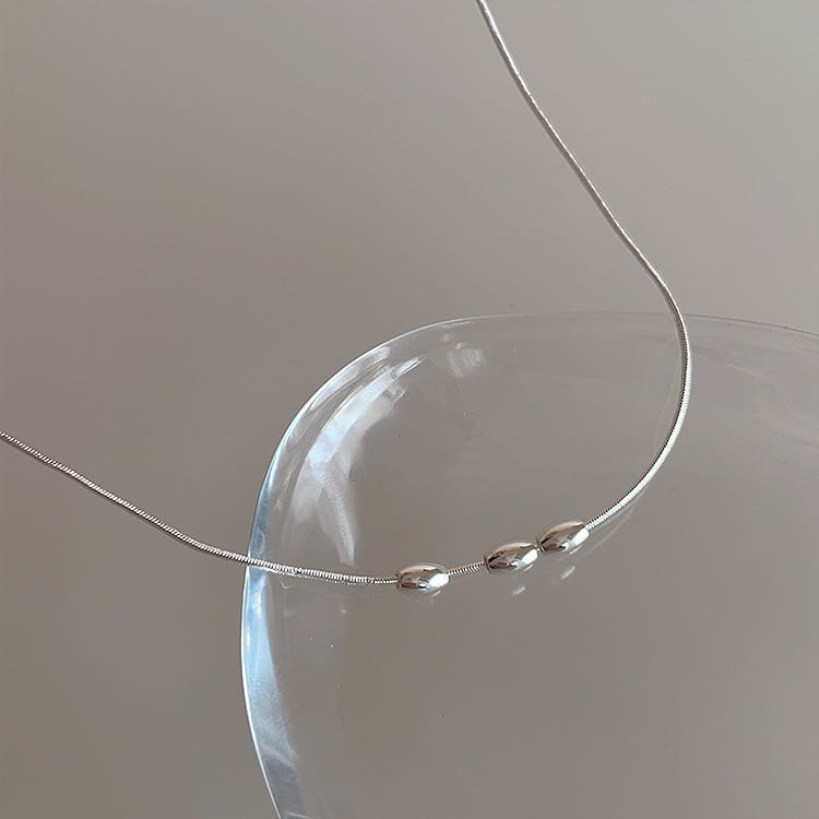 A delicate silver snake chain necklace with three smooth oval-shaped metallic beads from a set of five minimalist silver and pearl pendant necklaces.