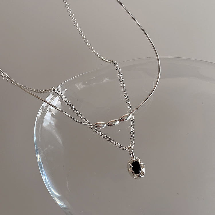 Silver necklace from a set of five minimalist silver and pearl pendant necklaces featuring a delicate chain and a black stone flower-shaped pendant.