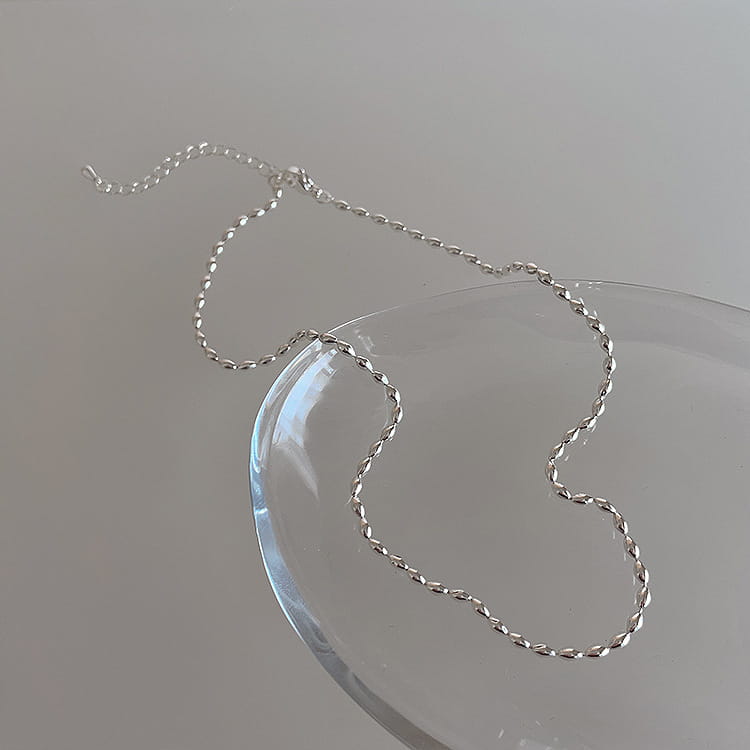 A delicate silver twisted chain necklace made of silver resting on a clear glass plate from a set of five minimalist silver and pearl pendant necklaces.