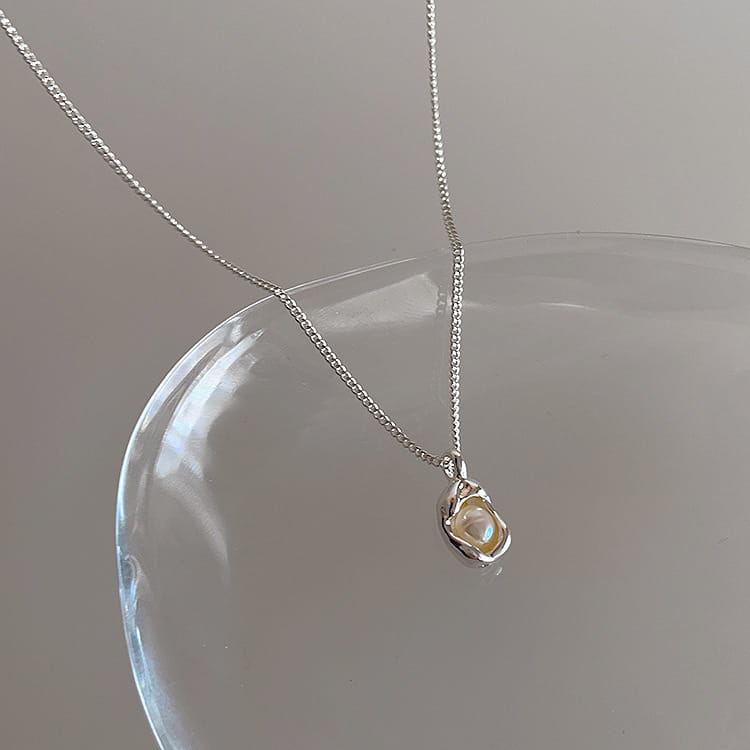 A delicate silver chain necklace from a set of five minimalist silver and pearl pendant necklaces featuring a small irregularly shaped silver pendant cradling a soft pearlescent bead.
