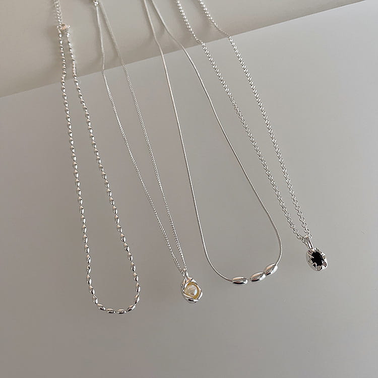 Set of five minimalist silver and pearl pendant necklaces featuring various chain styles including a twisted link design, a simple snake chain with three oval beads, and one necklace with a black gemstone.