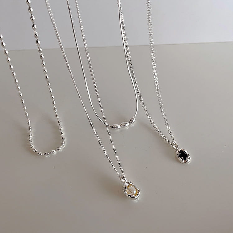 A set of five minimalist silver necklaces featuring unique chain styles and pearl pendants in a cage setting.