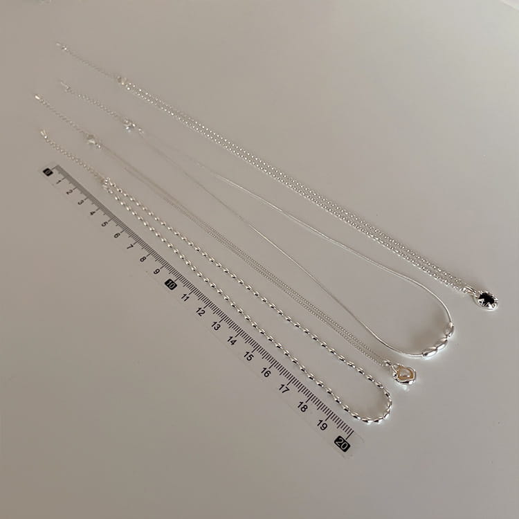 set of five minimalist silver chain necklaces with delicate links and small pearl pendants displayed alongside a ruler for scale.