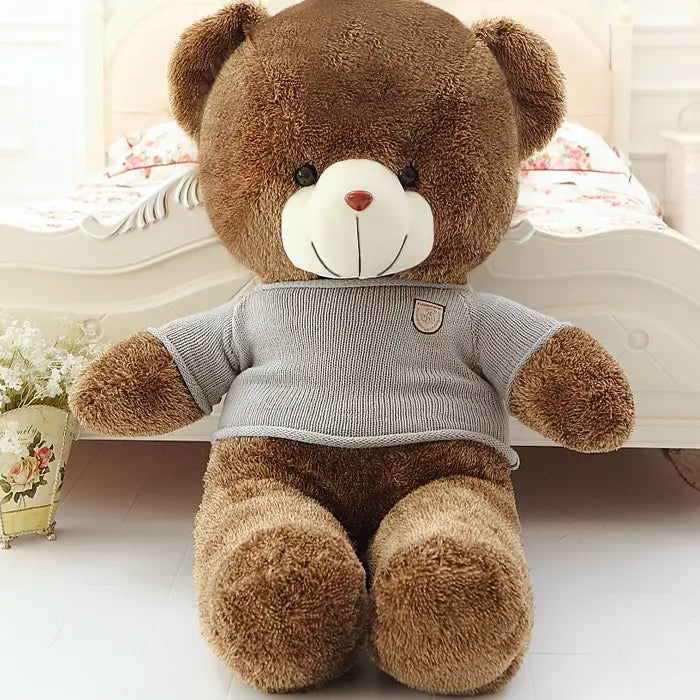 A plush brown teddy bear stuffed animal for kids wearing a gray knitted sweater with a small chest patch available in sizes 40 to 200 centimeters.
