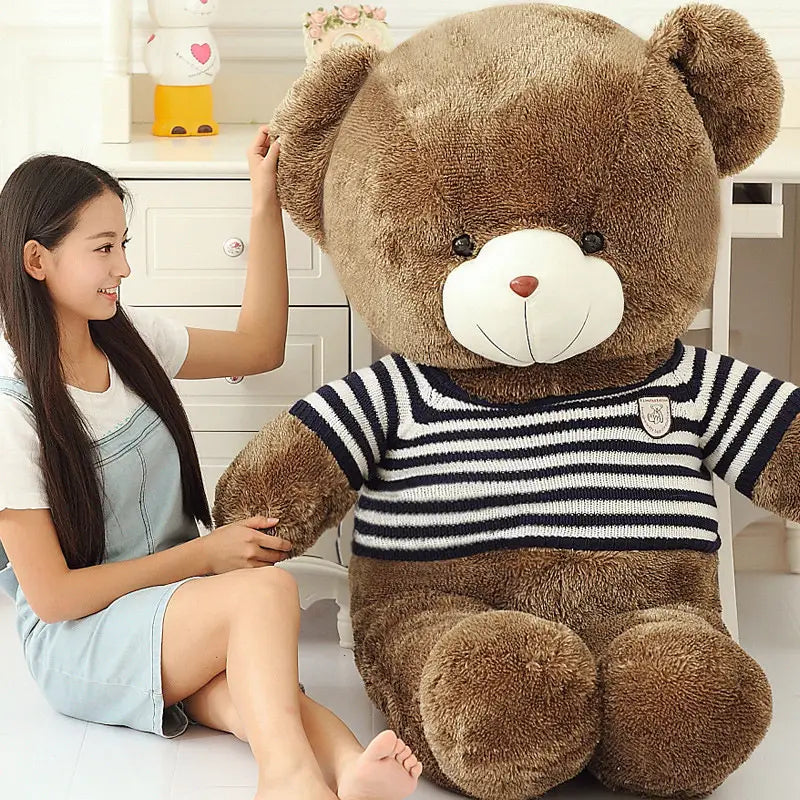 A plush brown teddy bear wearing a black and white striped knit sweater with a small emblem on the chest suitable as a stuffed animal toy for kids measuring 40 to 200 cm.