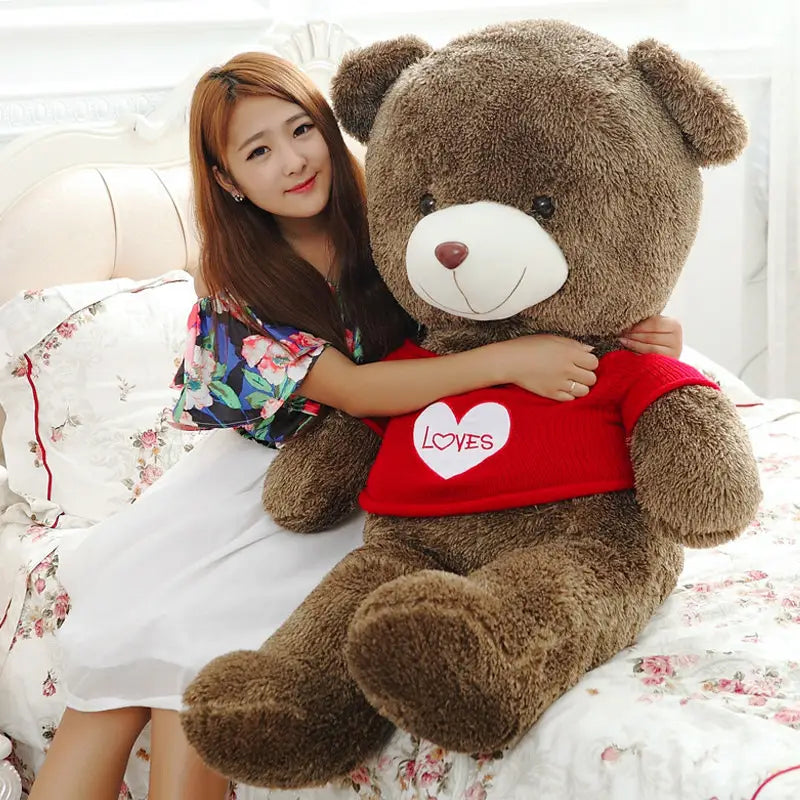 Brown plush teddy bear wearing a red shirt with a white heart and loves embroidered on it is a stuffed animal toy for kids available in sizes 40 to 200 cm.