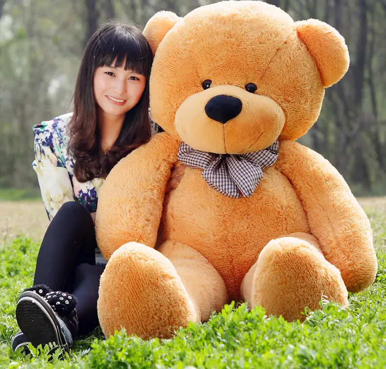 A plush tan-colored teddy bear stuffed animal for kids featuring a black nose button eyes and a checkered bow tie available in sizes 40 to 200 cm.