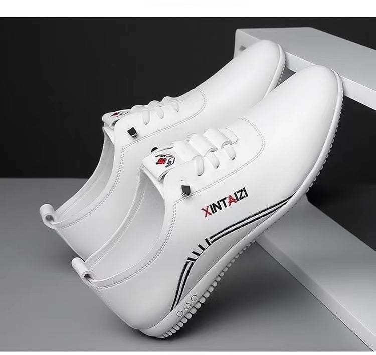 Zapatillas planas casuales de cuero blanco con costuras negras y un logotipo rojo en el lateral, diseñadas para una comodidad ligera y transpirable.