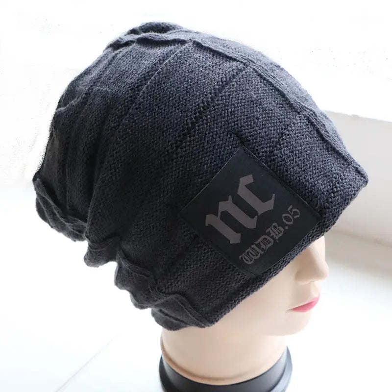 Men’s fleece lined knitted winter beanie hat in black featuring a textured slouchy design and a rectangular patch with stylized lettering.