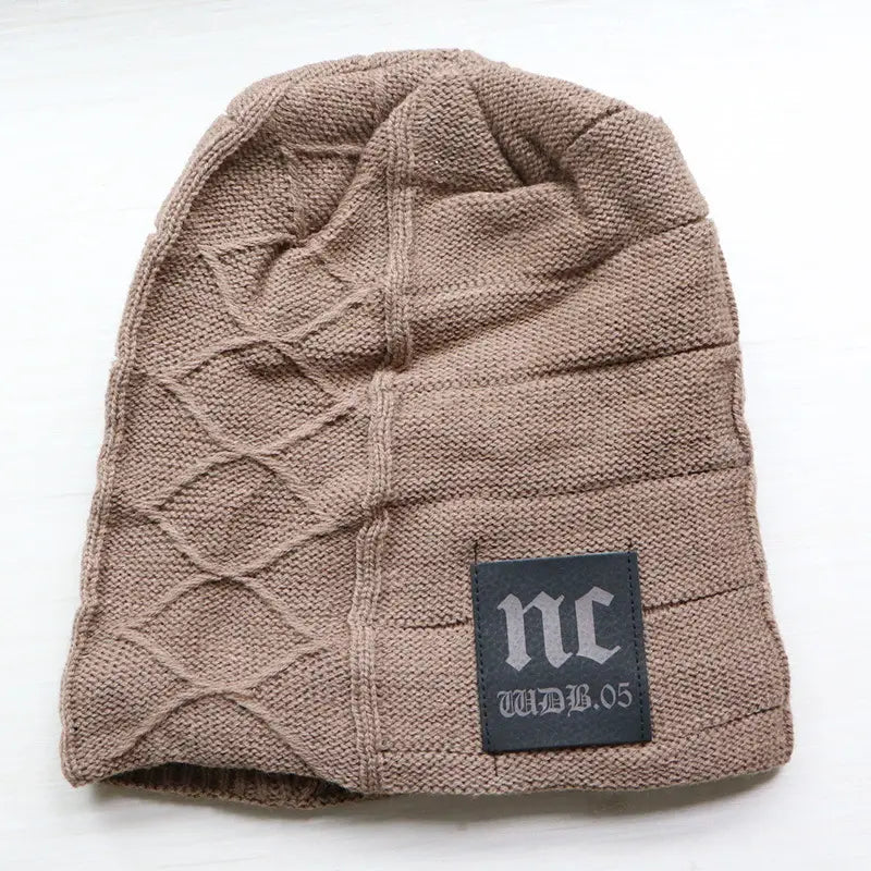 A taupe men’s fleece lined knitted winter beanie hat with a diamond-patterned cable knit design and a black leather patch featuring the nc logo.