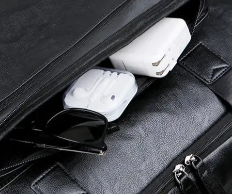 Men’s pu leather travel duffel bag in black with zipper compartments containing white charging adapters and sunglasses.