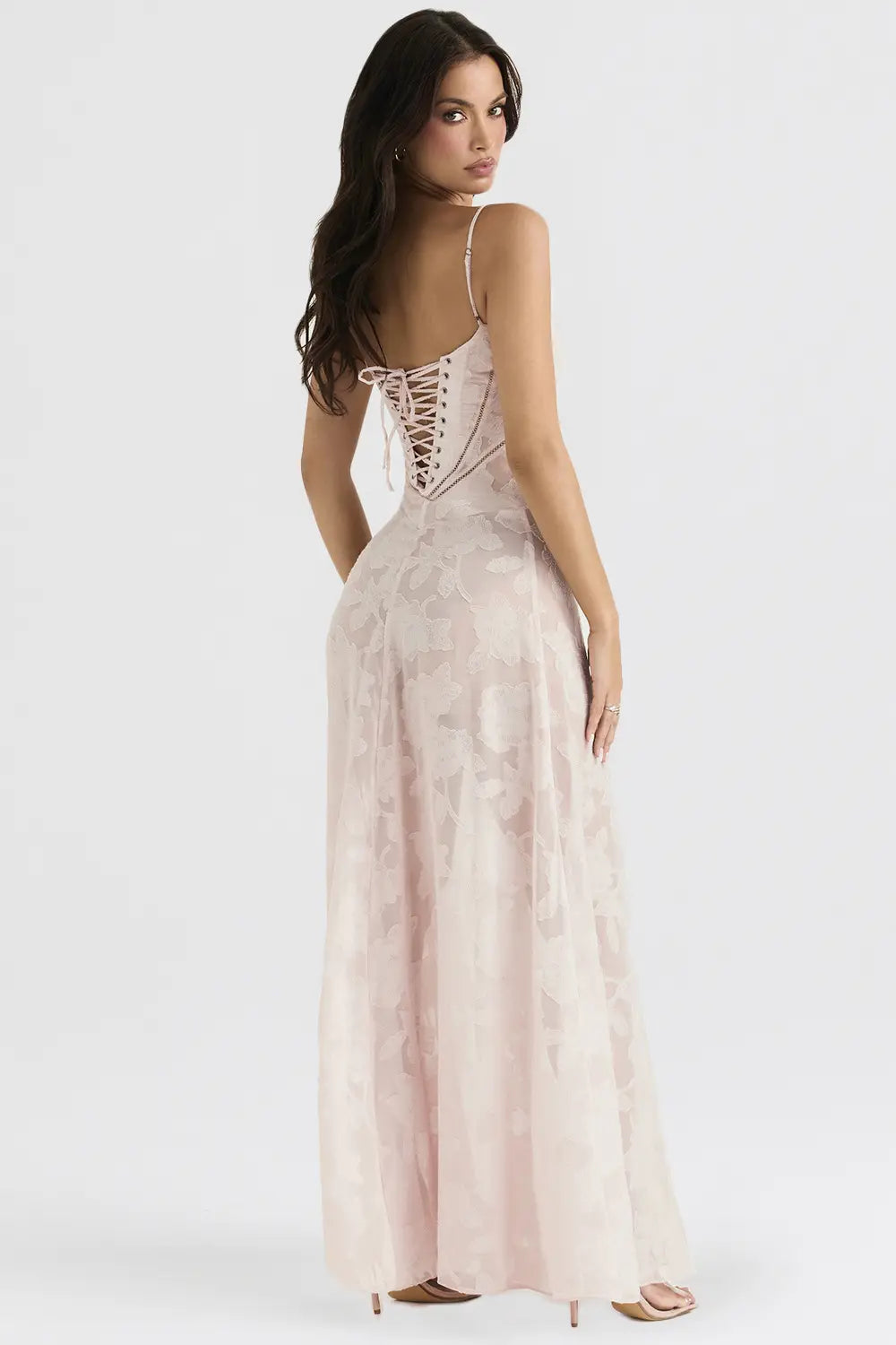 Une délicate robe de soirée maxi en dentelle florale rose blush sans dos, présentant un dos de style corset et de fines bretelles spaghetti, illustrée depuis la face arrière.