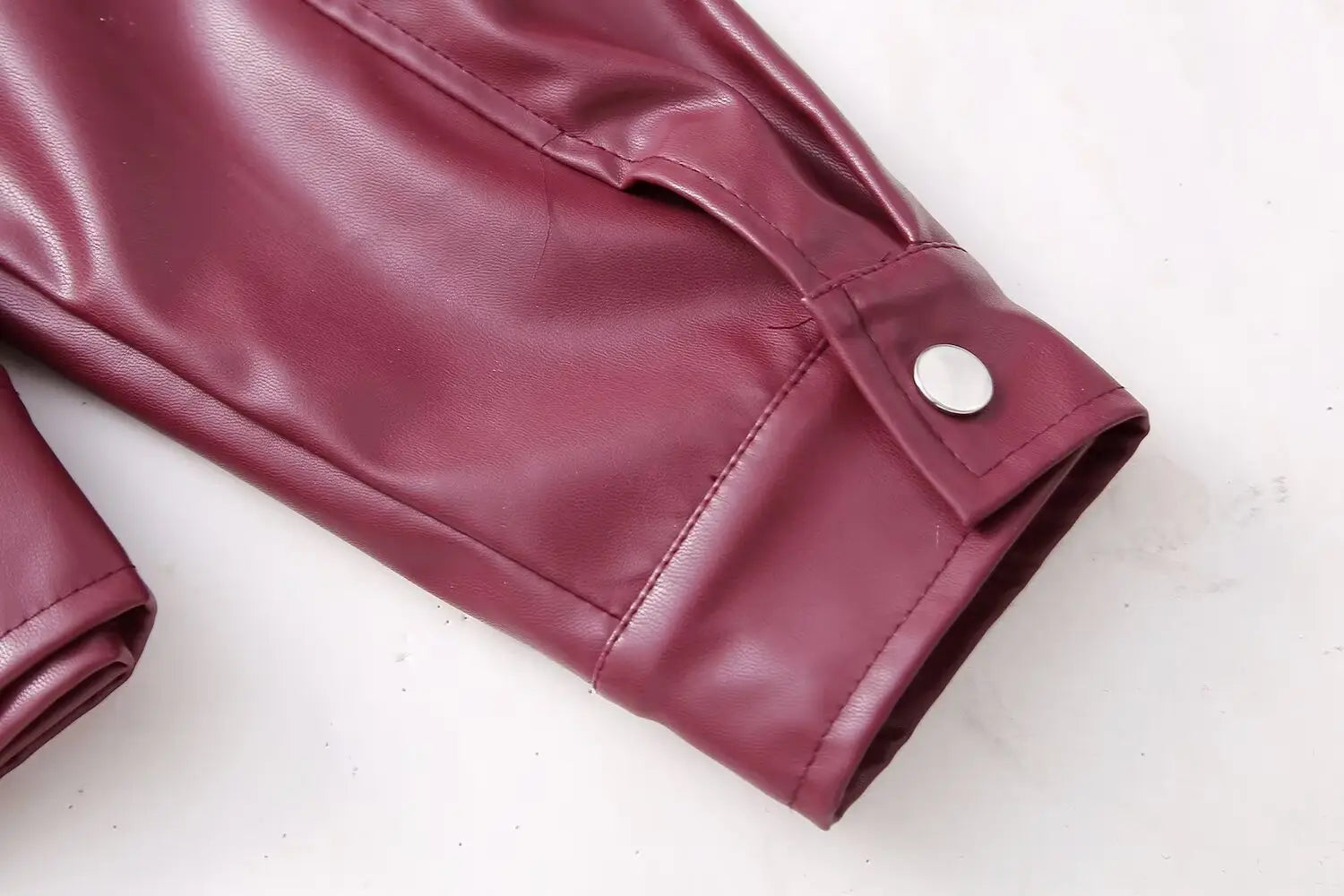 Maroon faux leather biker jacket for women featuring a sleeve with a silver button closure.