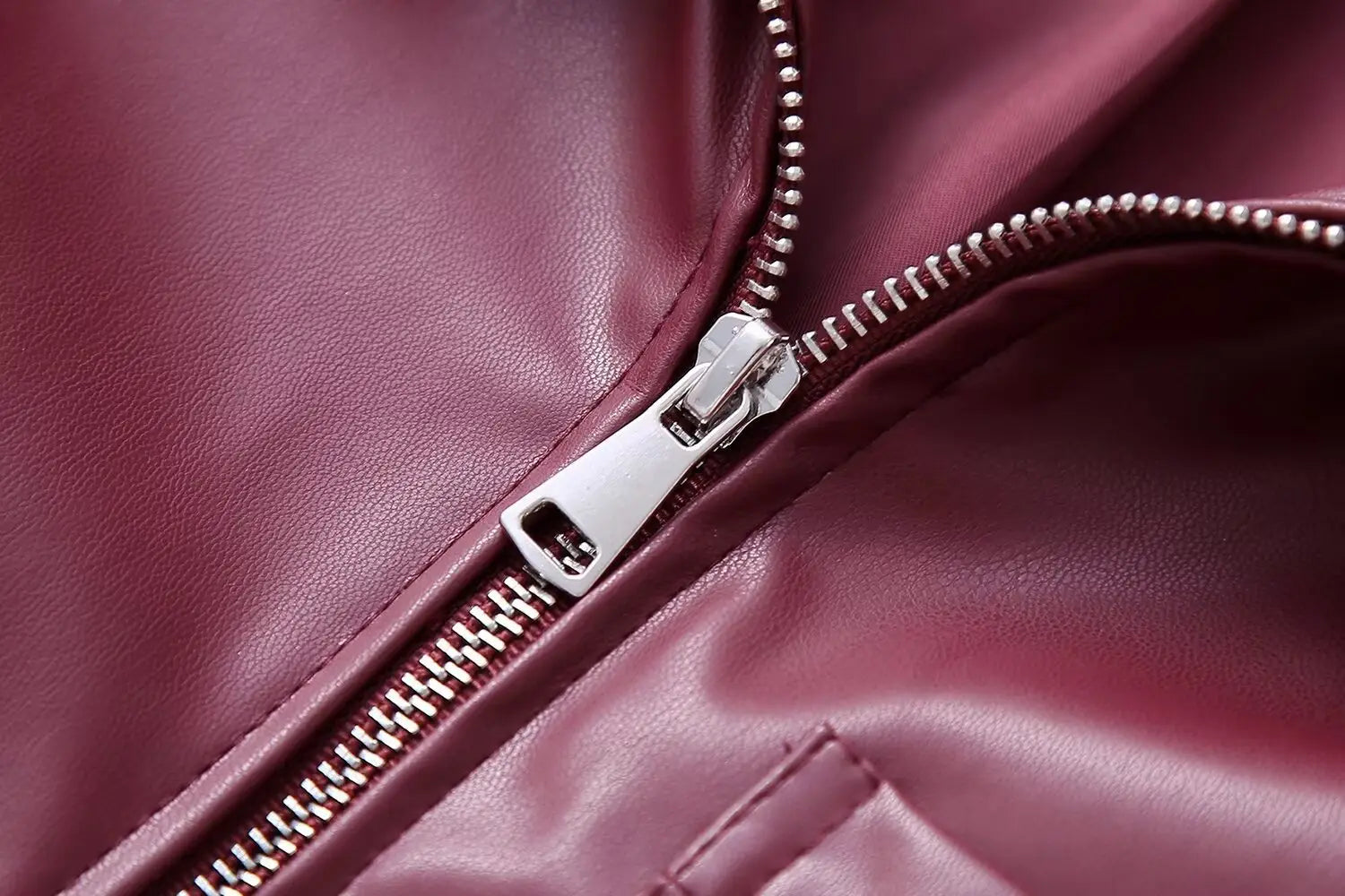 A close-up of a silver zipper with metallic teeth and pull tab on a maroon faux leather biker jacket for women.