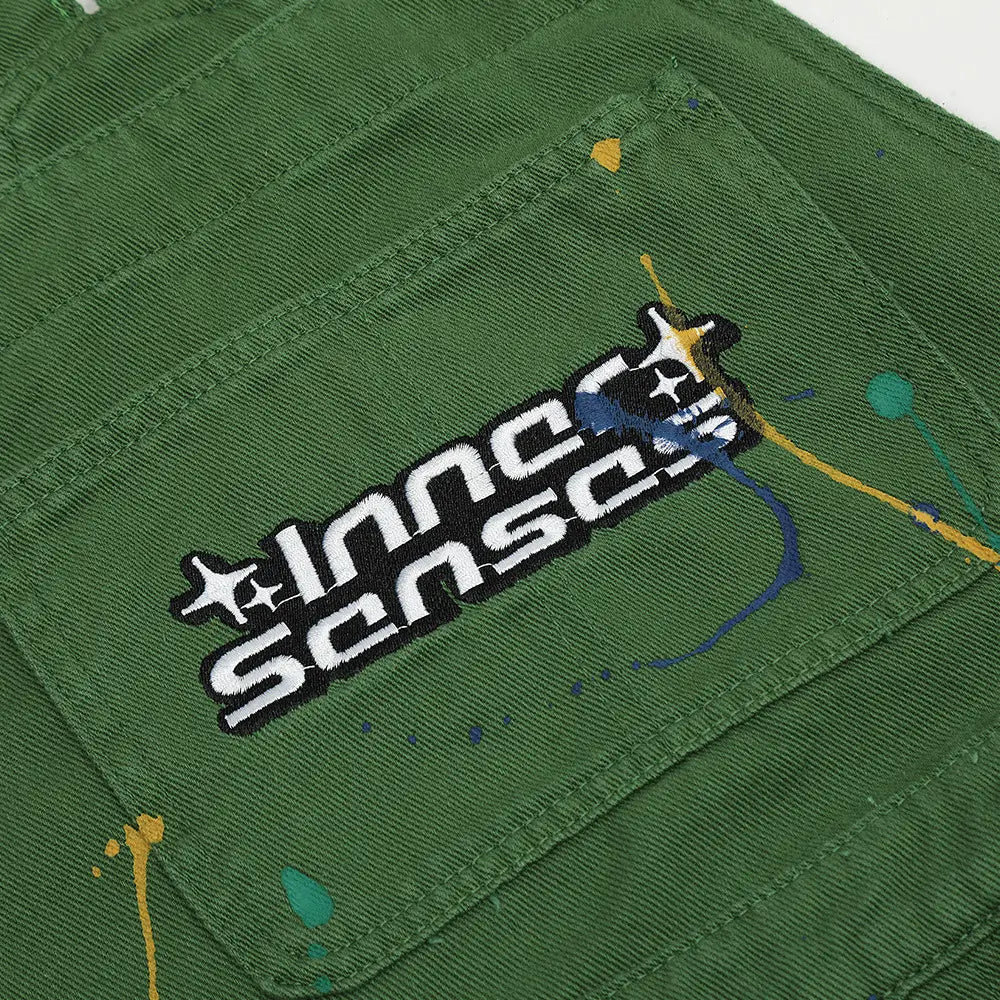 Grüne Cord-Latzhose mit Paint-Splatter-Logo, mit schwarzem und weißem Innsens-Logo-Patch sowie farbigen Farbspritzern als Akzenten