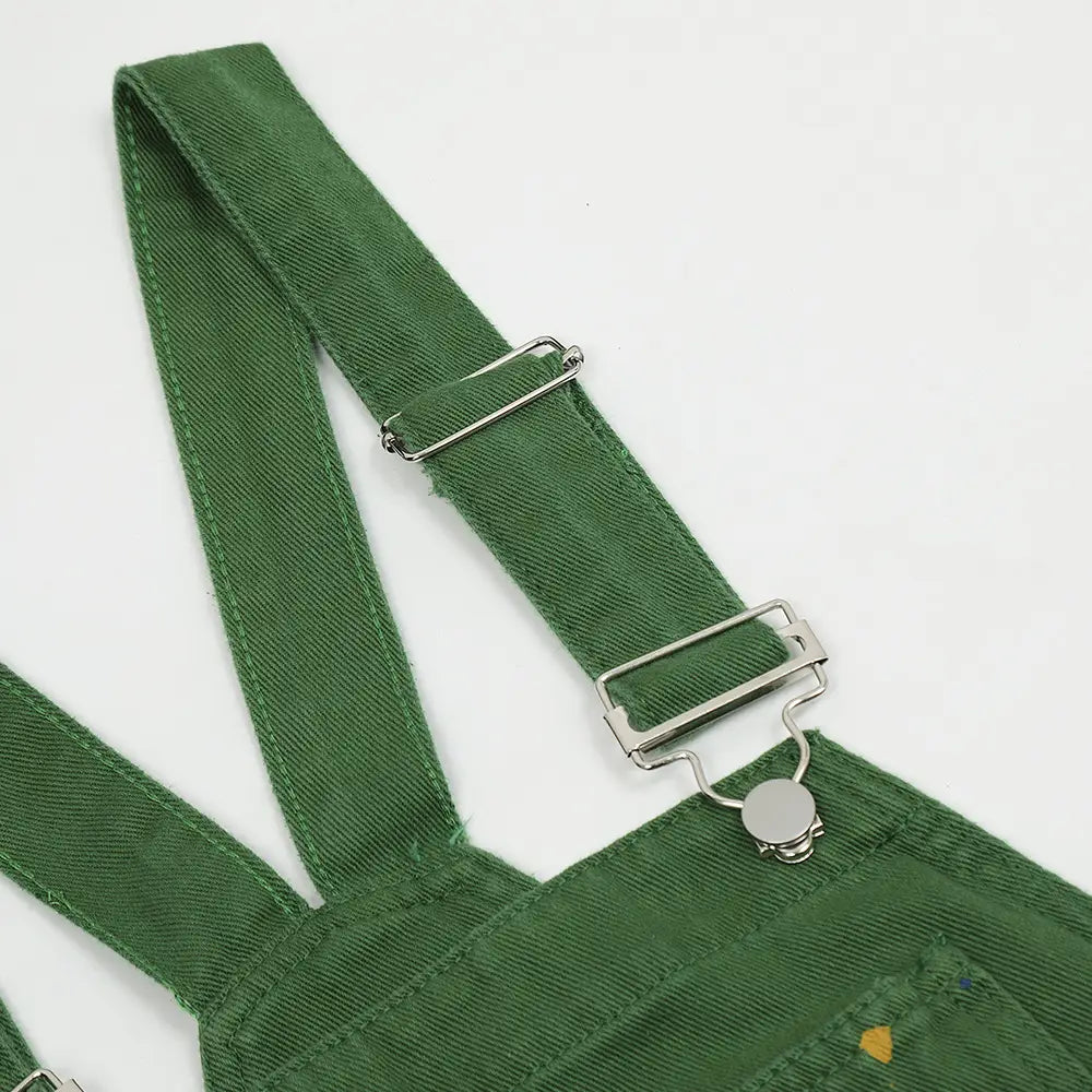 Grüne Jeans-Latzhose mit Paint-Splatter-Logo, silbernen Metallverschlüssen und verstellbaren Trägern aus robustem Denim-Material.