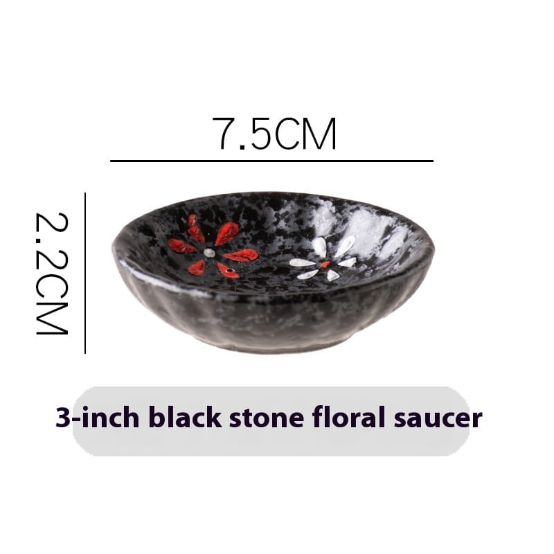 Un bol à condiments en céramique noir, avec une surface texturée, présentant des motifs floraux rouge et blanc peints à la main pour servir des en-cas.