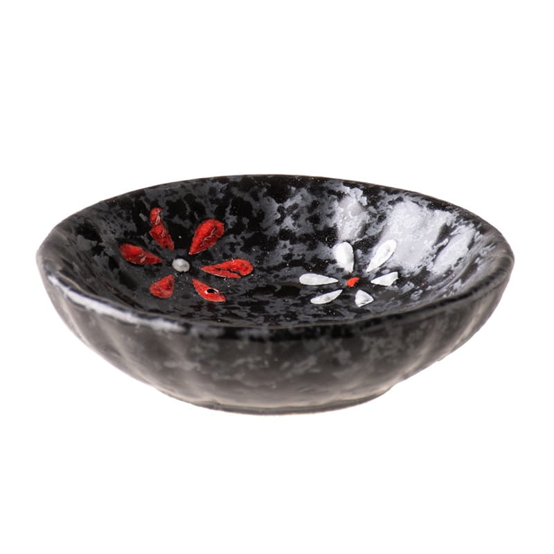 Un bol à condiments en céramique noir, avec une surface texturée mouchetée, peint à la main de fleurs rouges et blanches à l’intérieur, pour servir des en-cas.