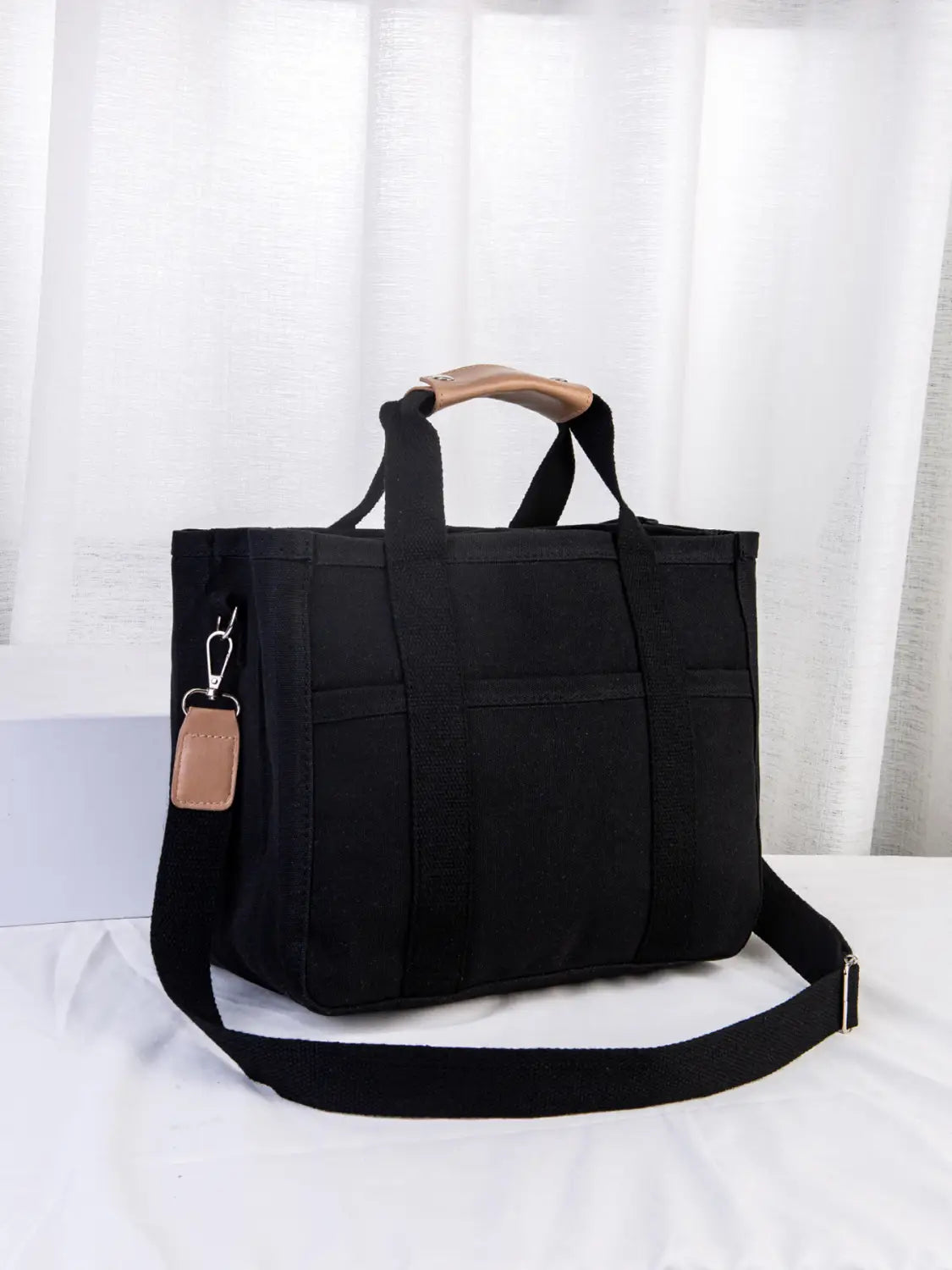 Black canvas messenger bag with tan leather handles and a matching strap tag designed as a mother and baby travel tote.