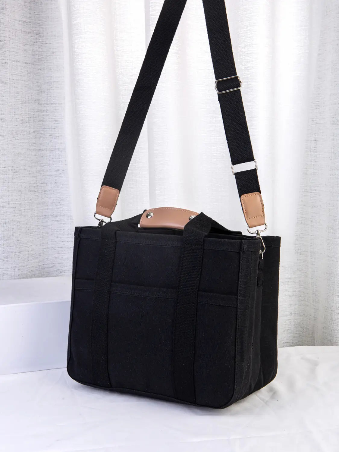Black canvas messenger bag with tan leather accents and adjustable shoulder strap designed for mother and baby travel tote use.