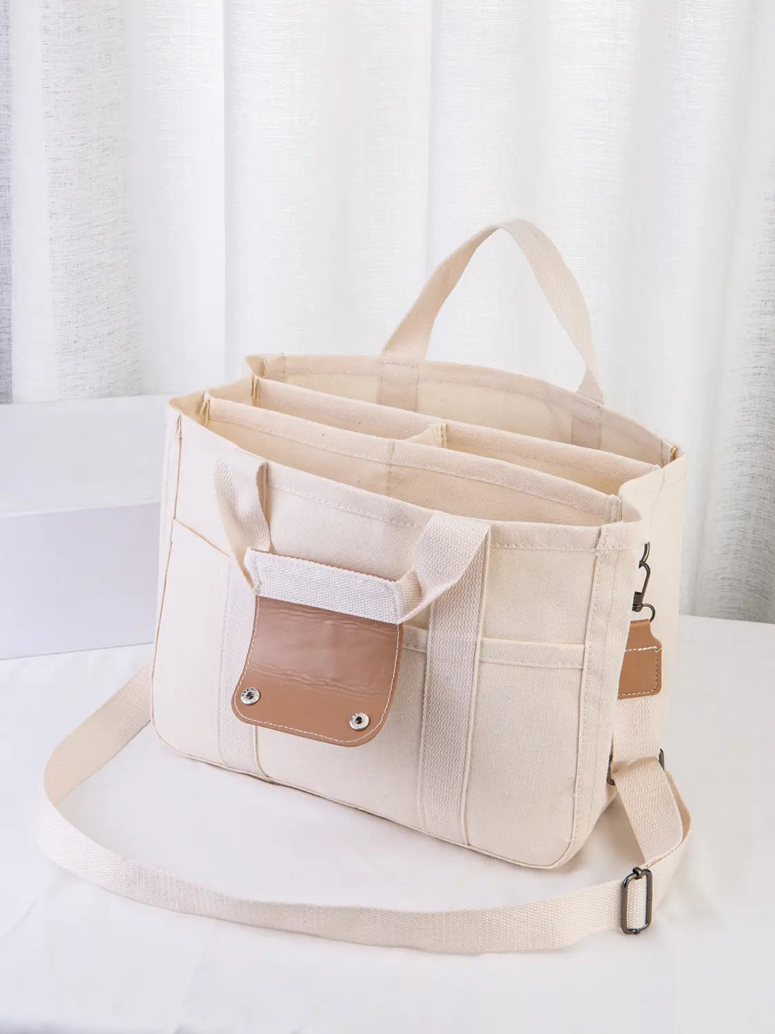 Beige canvas messenger bag with tan leather accents and a detachable shoulder strap designed as a mother and baby travel tote.