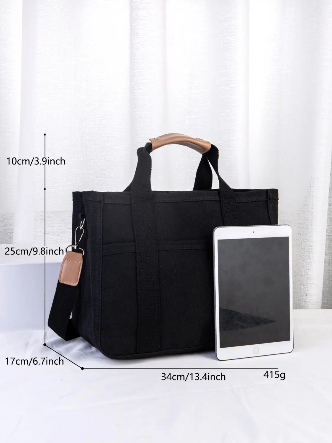 Black canvas messenger bag with tan leather handles and matching strap featuring multiple pockets for organized storage ideal for mother and baby travel.