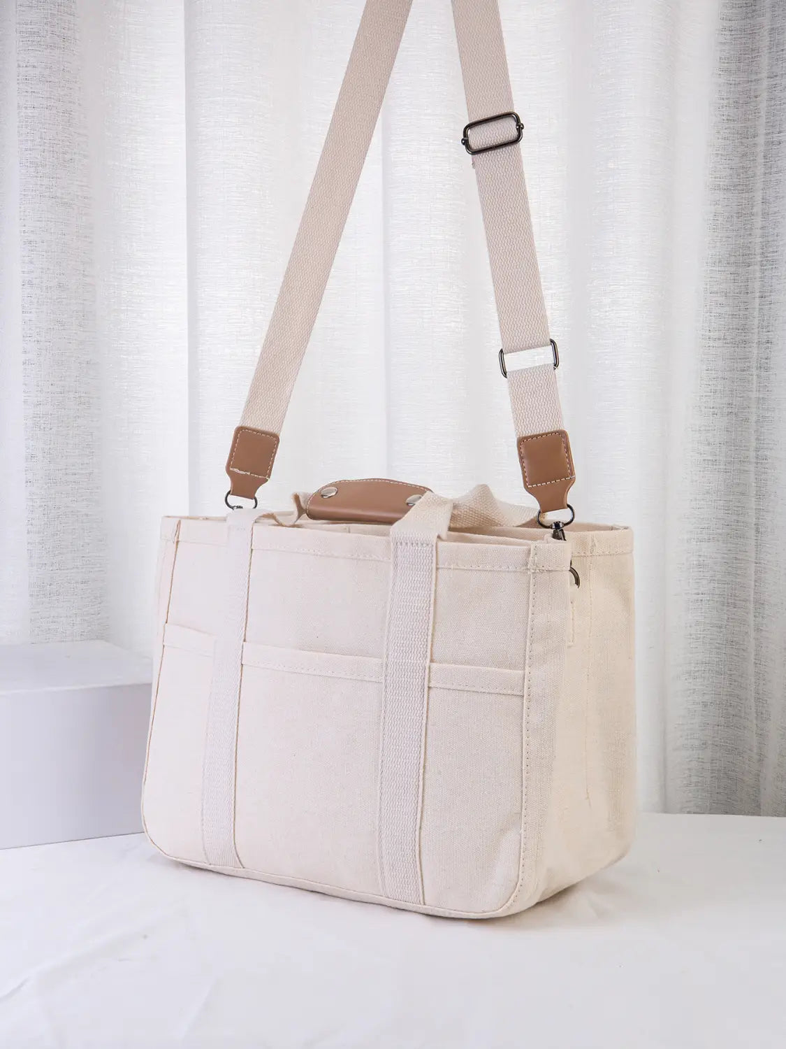 beige canvas messenger bag with tan leather accents and adjustable shoulder strap designed as a mother and baby travel tote