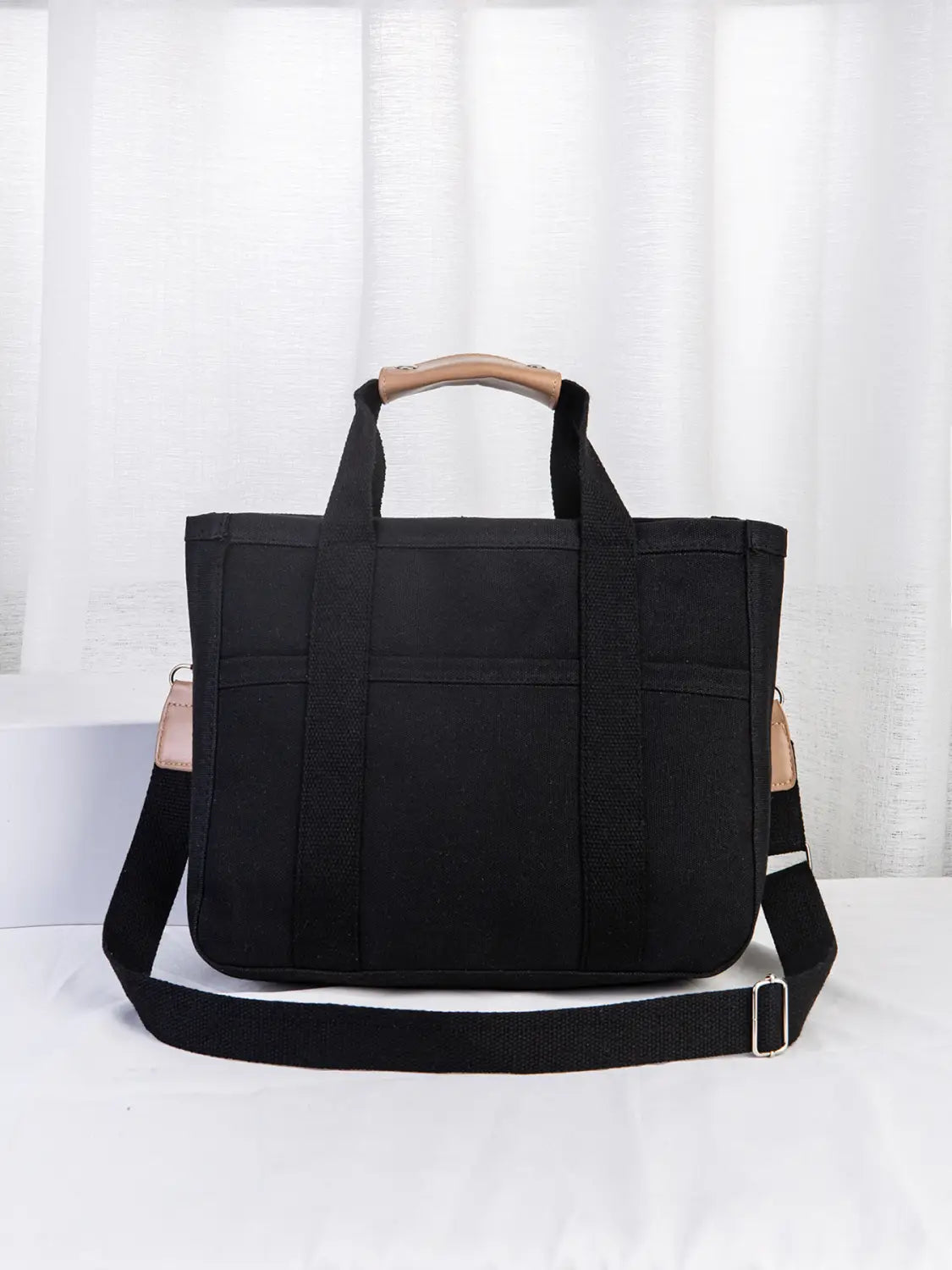 Black canvas messenger bag with tan leather handles and shoulder strap accents designed as a mother and baby travel tote.