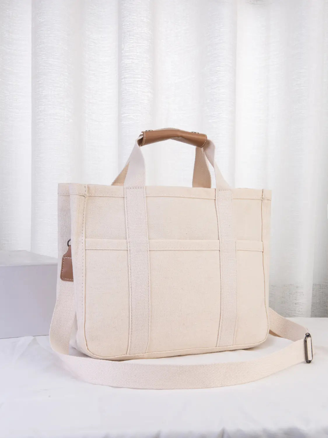 Beige canvas messenger bag with tan leather handles and adjustable strap designed as a mother and baby travel tote.