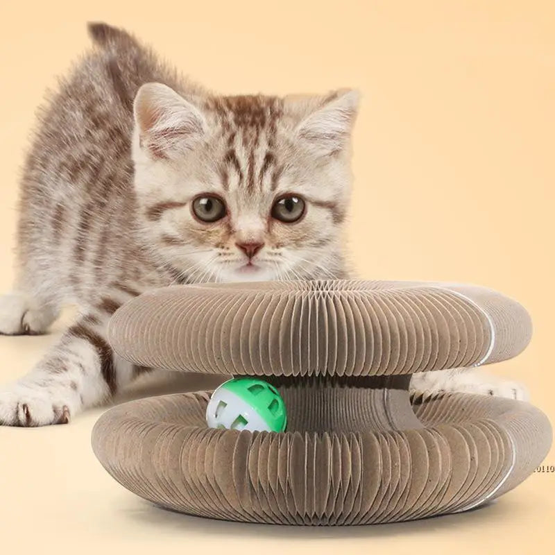 Tablero rascador de cartón corrugado beige para gatos, tipo juguete con forma de órgano, con una pelota verde y blanca con campana en su interior para el entretenimiento felino.