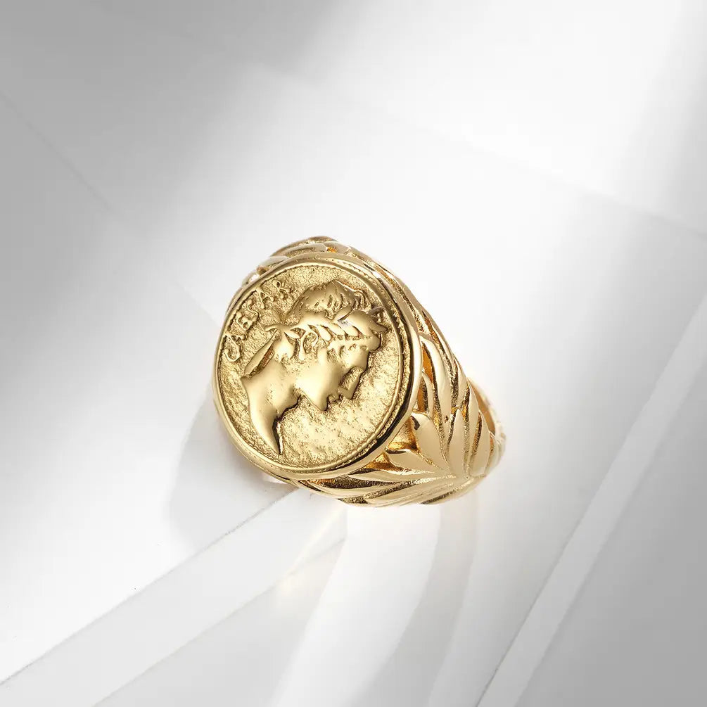 Gold-colored stainless steel vintage Caesar portrait signet ring with an embossed classical profile on a circular face and intricate leaf-patterned band details.