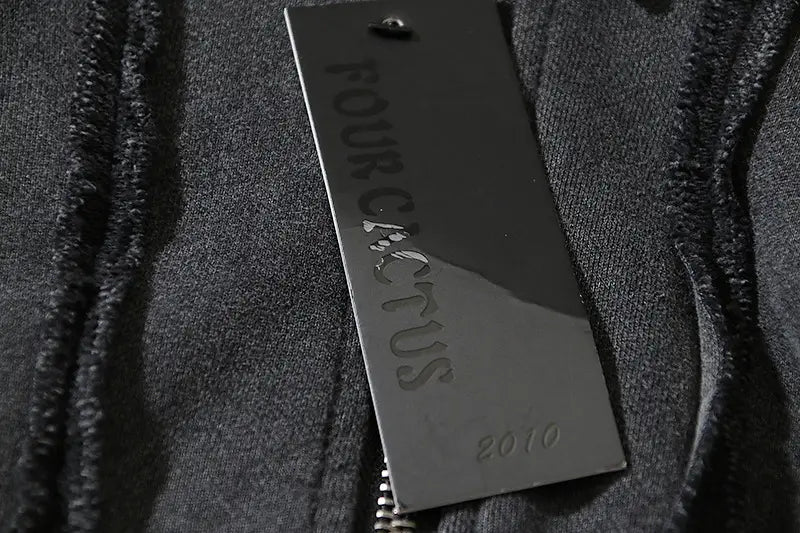 Una etiqueta rectangular negra mate y elegante con el nombre de la marca Four Cactus en relieve y el año 2010 grabado debajo en una sudadera con cremallera y capucha estilo batik desgastado.