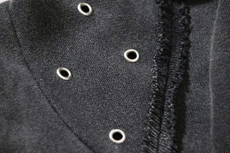 Chaqueta de denim negra con ojales plateados a lo largo de la costura del hombro, mostrada desde la parte trasera, combinada con un cárdigan con cremallera y capucha estilo batik desgastado.