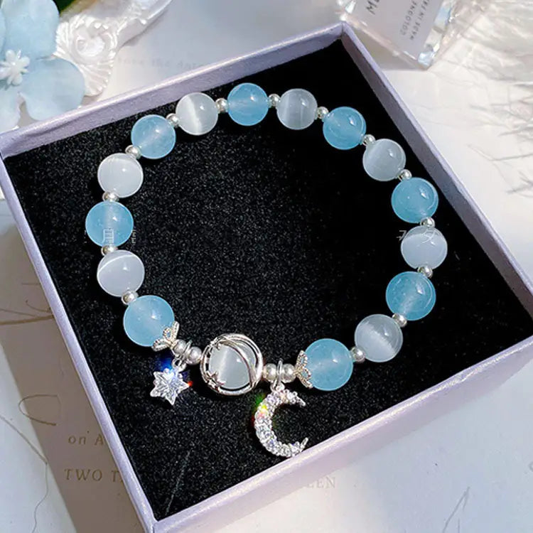 A handmade celestial moon and star crystal bead bracelet featuring alternating light blue and translucent white cat’s eye stones accented with silver-toned crescent moon and star charms.