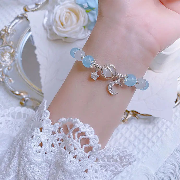 A delicate handmade celestial moon and star crystal bead bracelet featuring light blue and white translucent beads with silver-toned crescent moon and star charms.