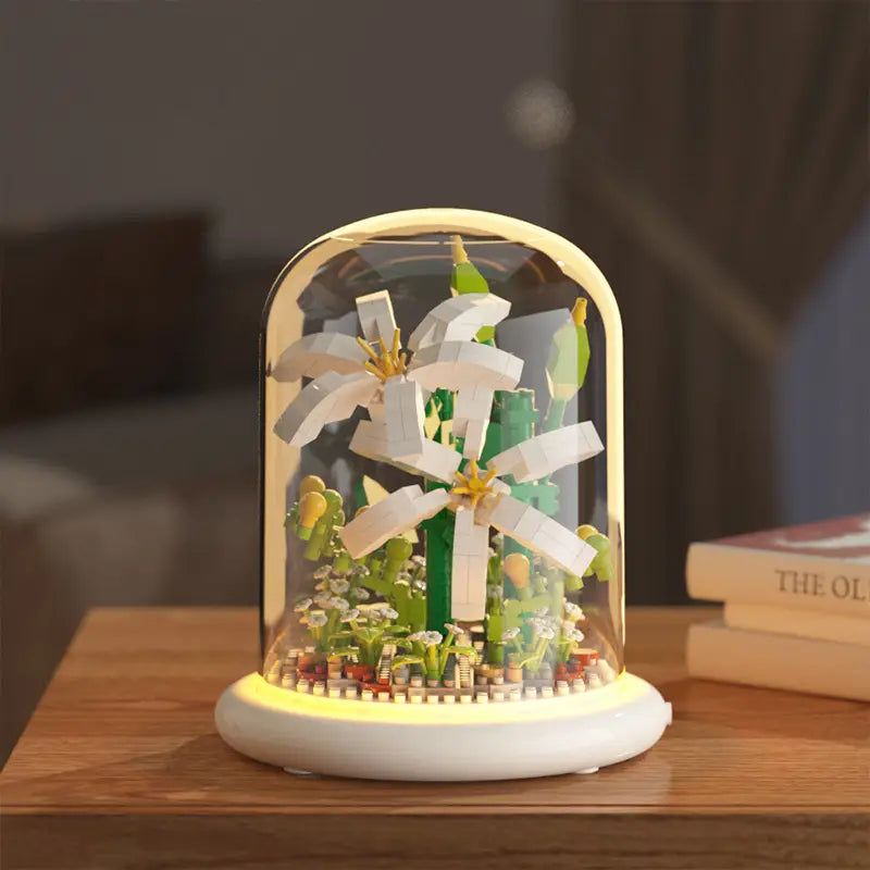 Un modèle de fleurs en briques LEGO blanc et vert représentant des lys, exposé sous une coupole en verre avec un éclairage à LED, comme décoration jouet de dôme en verre pour fleurs, bloc de construction.