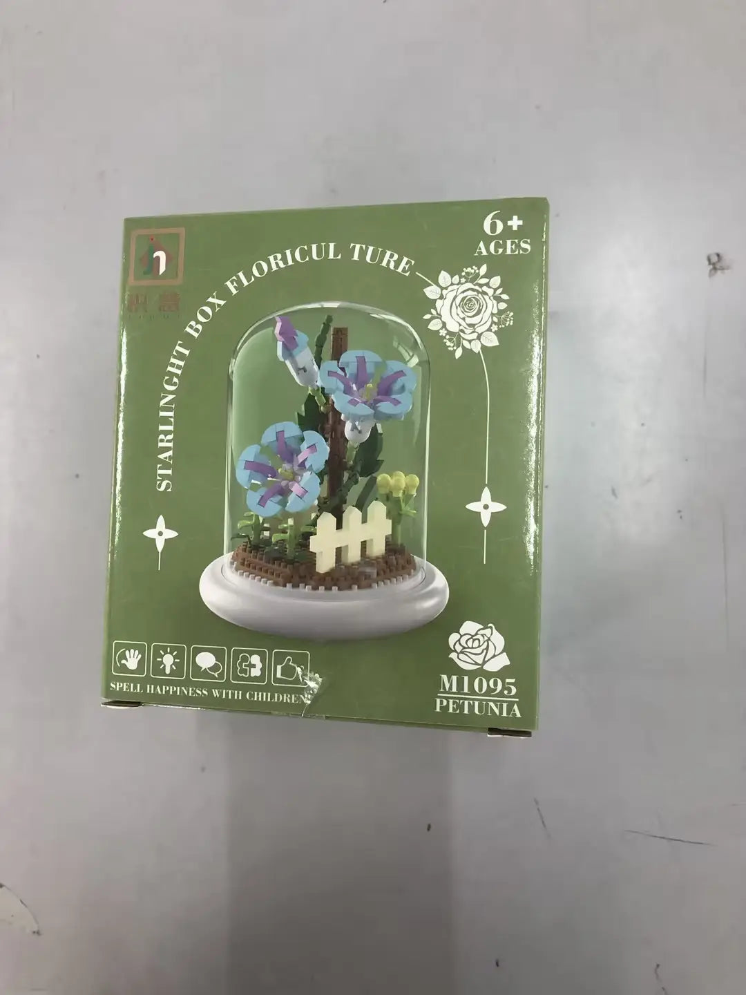 Boîte verte contenant un kit de construction floriculteur à starlight, avec des fleurs de pétunia violettes et bleues affichées sous une coupole en verre transparente, comme décoration jouet de dôme en verre pour fleurs, bloc de construction, éclairage LED.