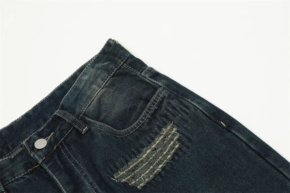 Jeans déchirés homme à effet usé, jambe droite, en denim de couleur foncée, comportant une pièce à l’aspect usé avec coutures visibles.