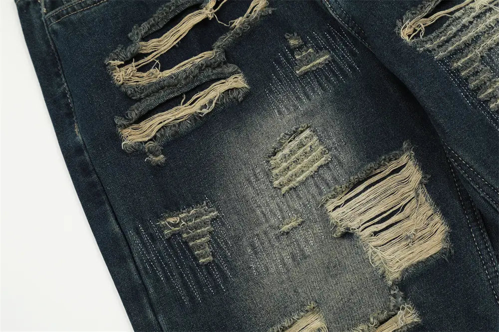 Jeans déchirés homme à effet usé, jambe droite, en denim, comportant plusieurs trous de déchirure effilochés avec coutures visibles et bords délavés.
