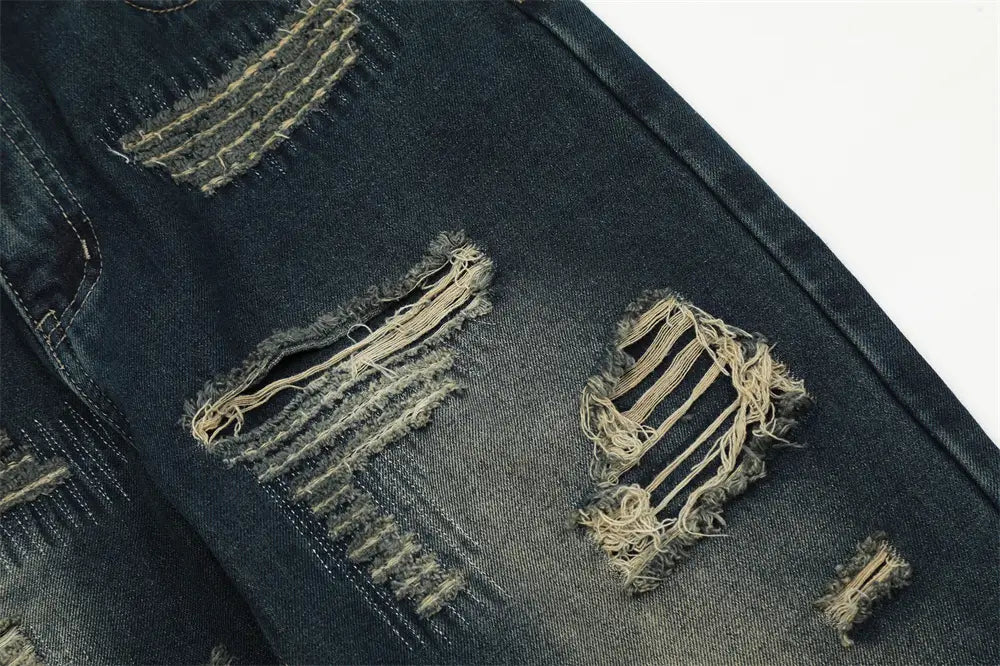 Jeans déchirés homme à effet usé, jambe droite, comportant des zones de déchirure effilochées avec coutures visibles et bords bruts.