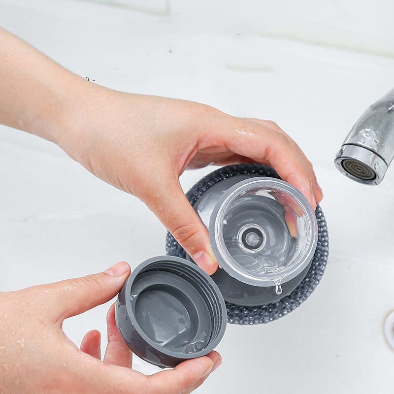Bouteille d’eau en plastique gris, avec couvercle et bouchon transparents, rincée sous un robinet qui coule dans un ensemble de brosse palmier distributeur de savon et de brosse à récurer.